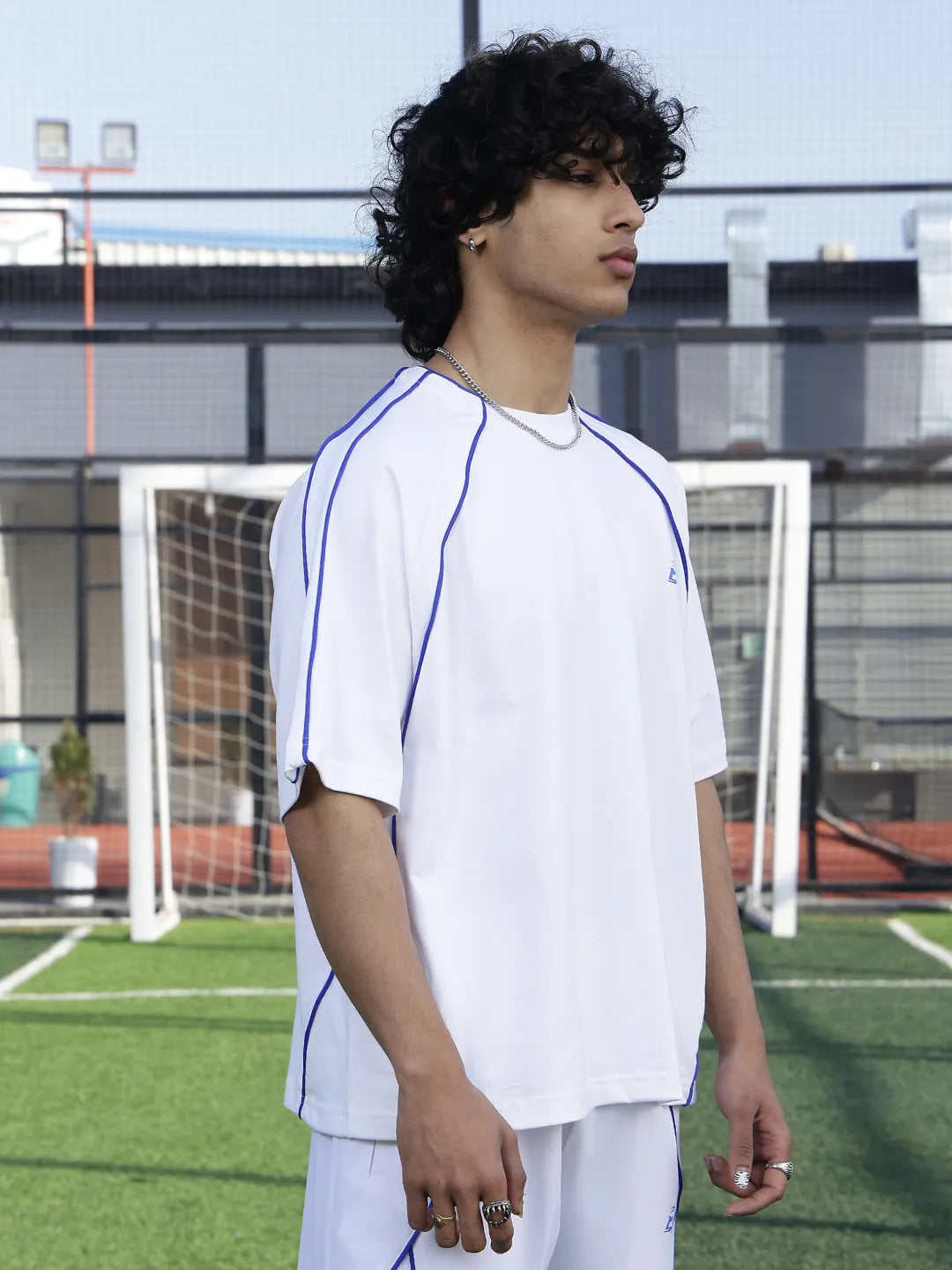 Person wearing a white baseball jersey with blue accents on a sports field.