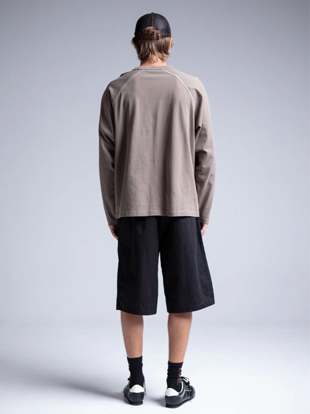A person wearing a taupe brown long-sleeve raglan t-shirt, black shorts, black socks, and black sneakers