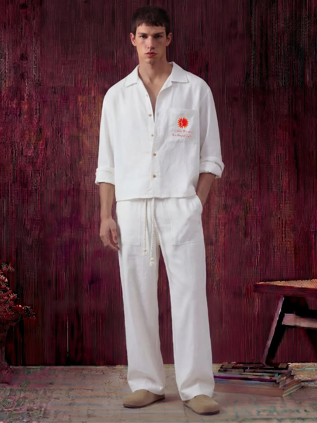 Man wearing a white outfit with a logo against a textured red-brown wall.