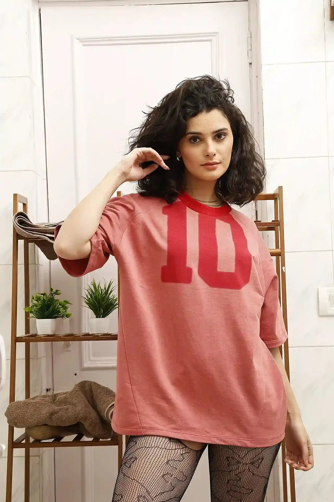 Woman wearing a pink oversized t-shirt with the number 10 on it, standing indoors.