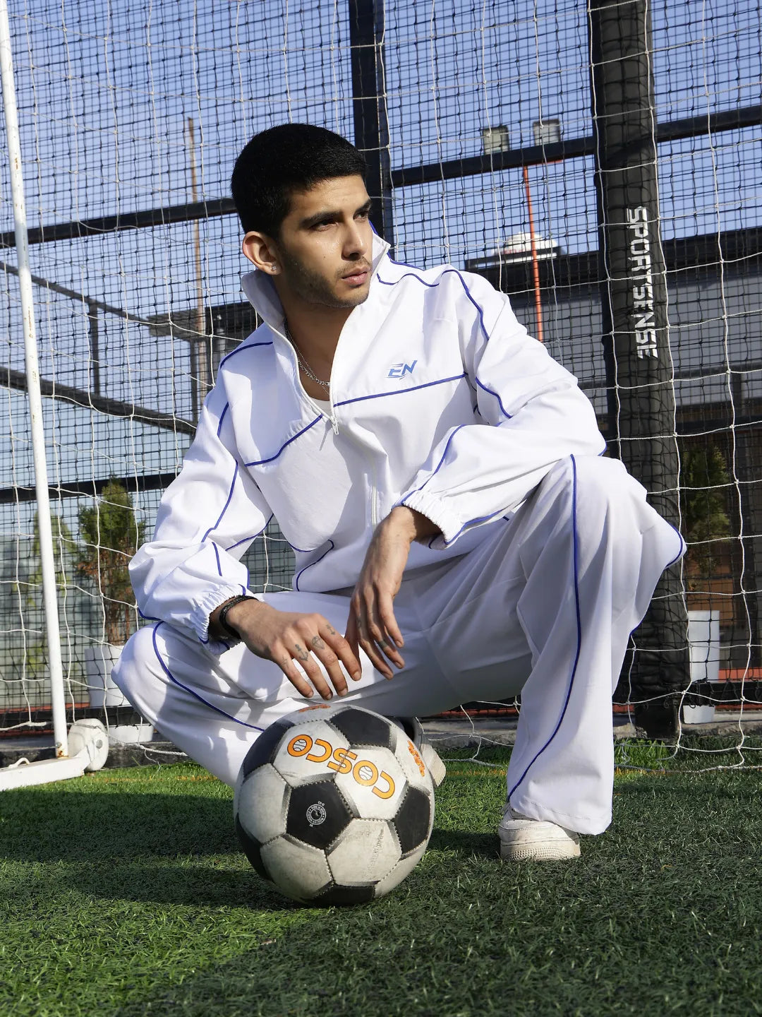Person in a white sports jacket  with a soccer ball on a grass field.