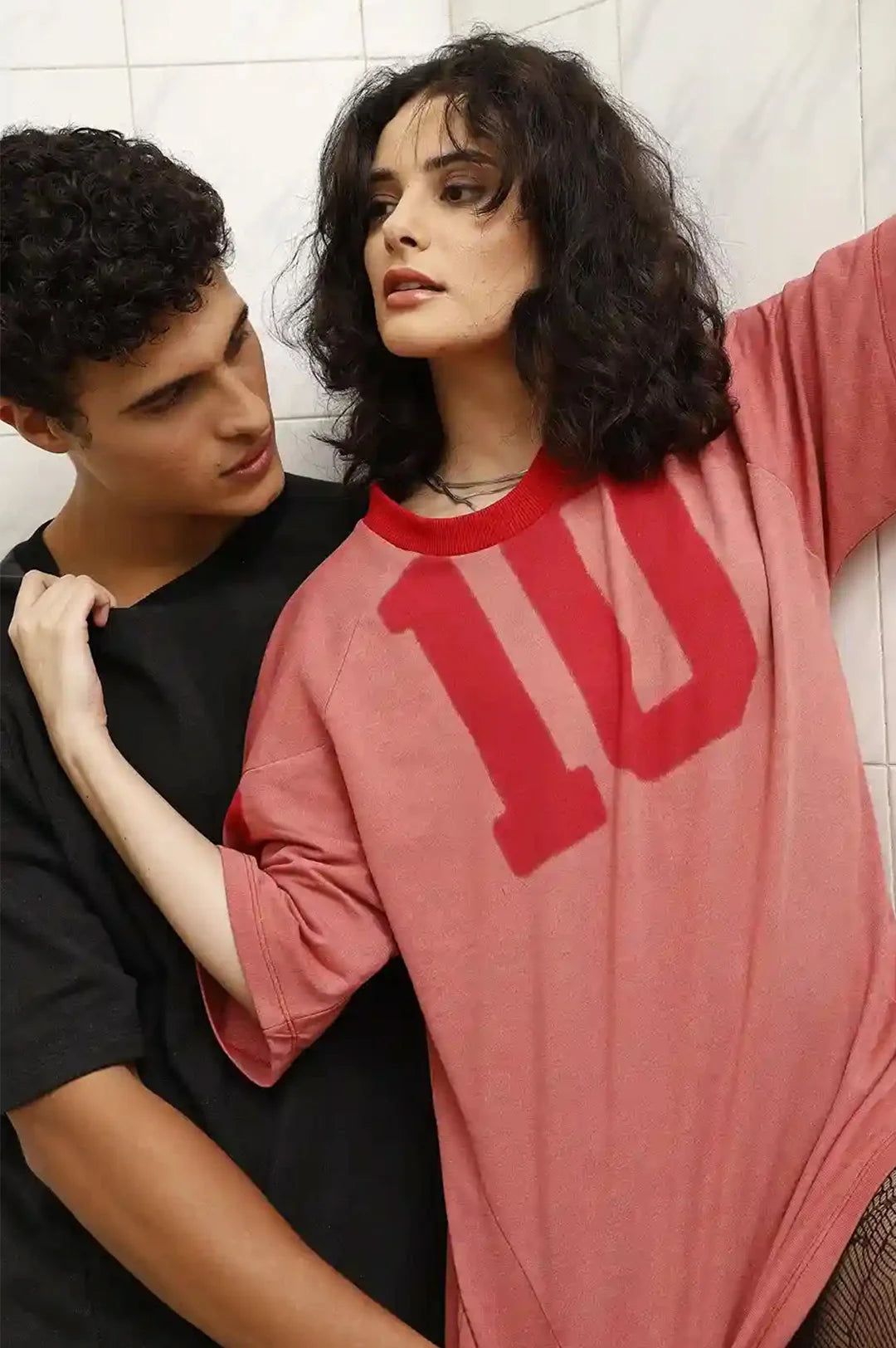 Two people standing close to each other against a tiled wall.