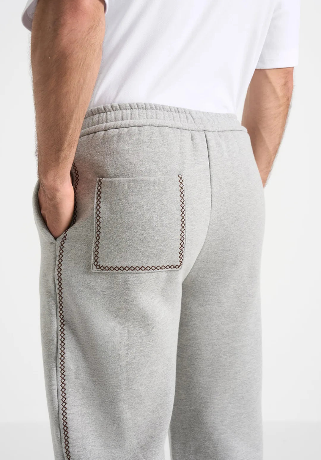 Man wearing a gray hoodie and dark pants, holding a brown bag on a white background