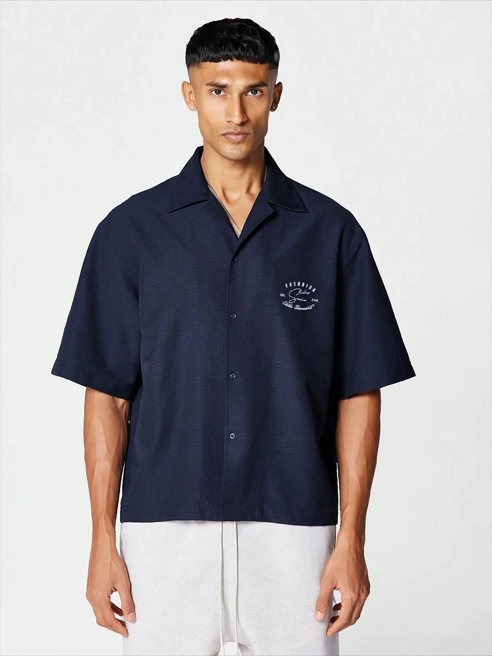 Man wearing a navy short-sleeve shirt with a logo on a white background