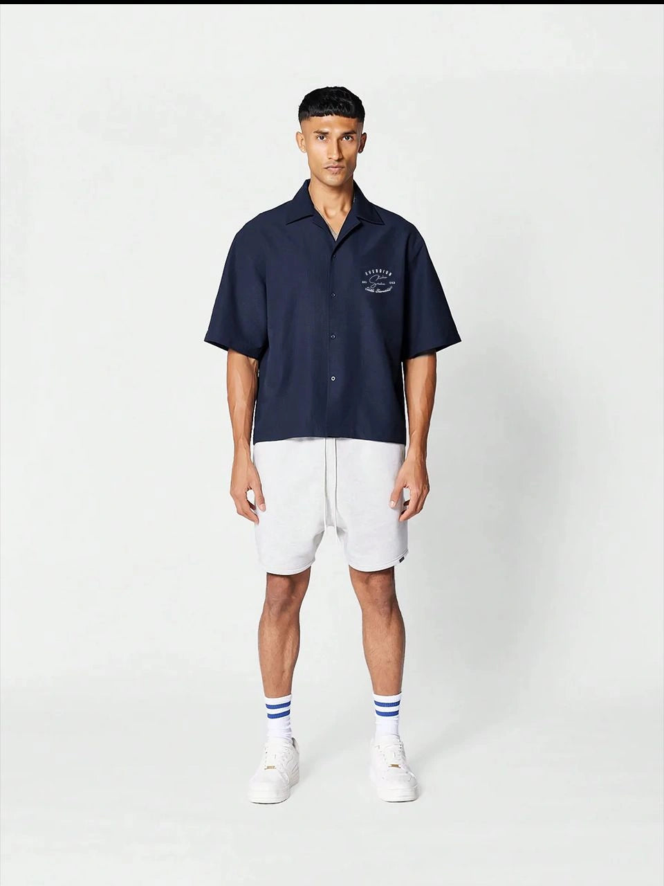 Man wearing a navy polo shirt and white shorts on a white background