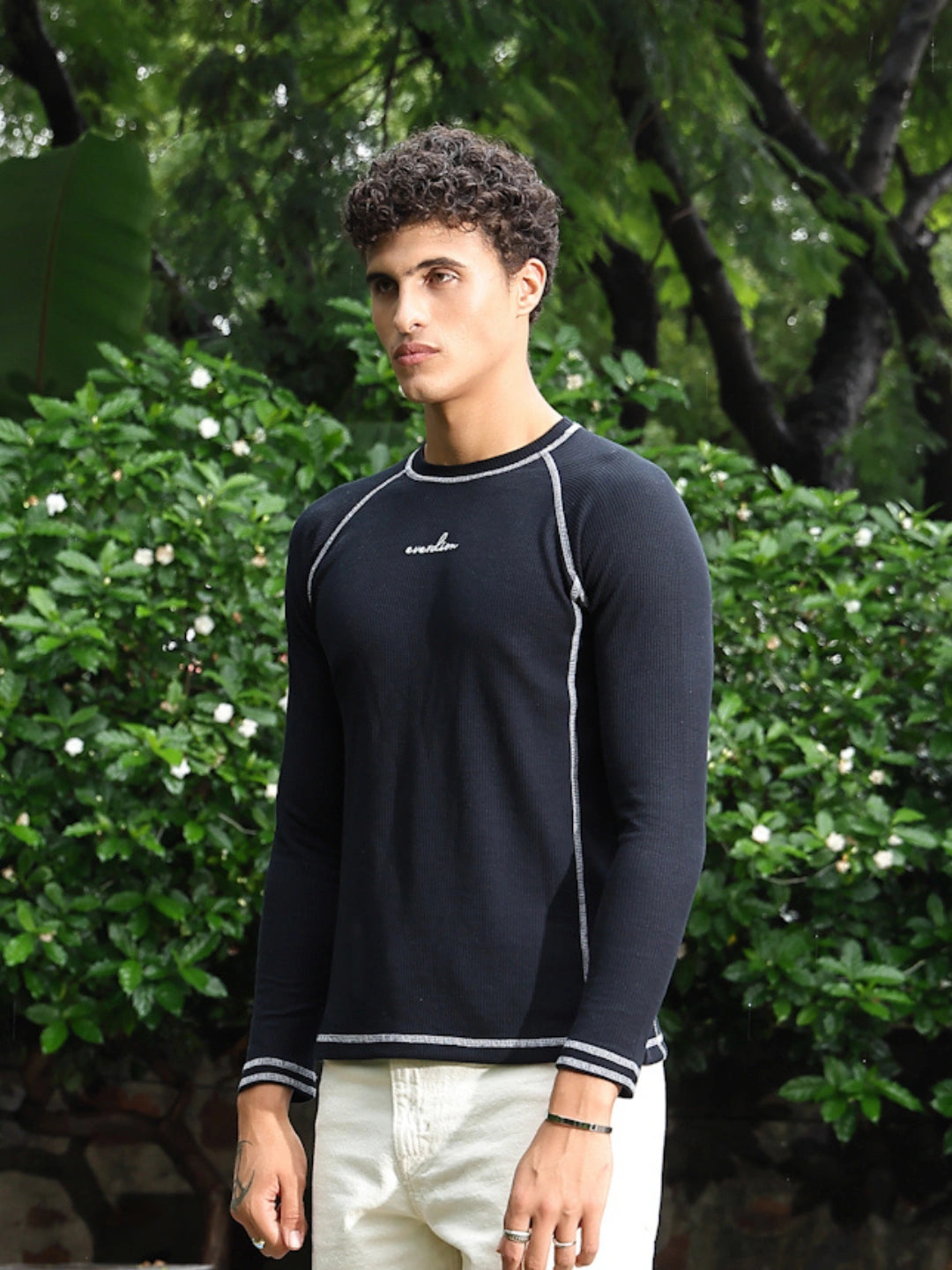 Man wearing a navy long-sleeve shirt with white trim standing outdoors among greenery.