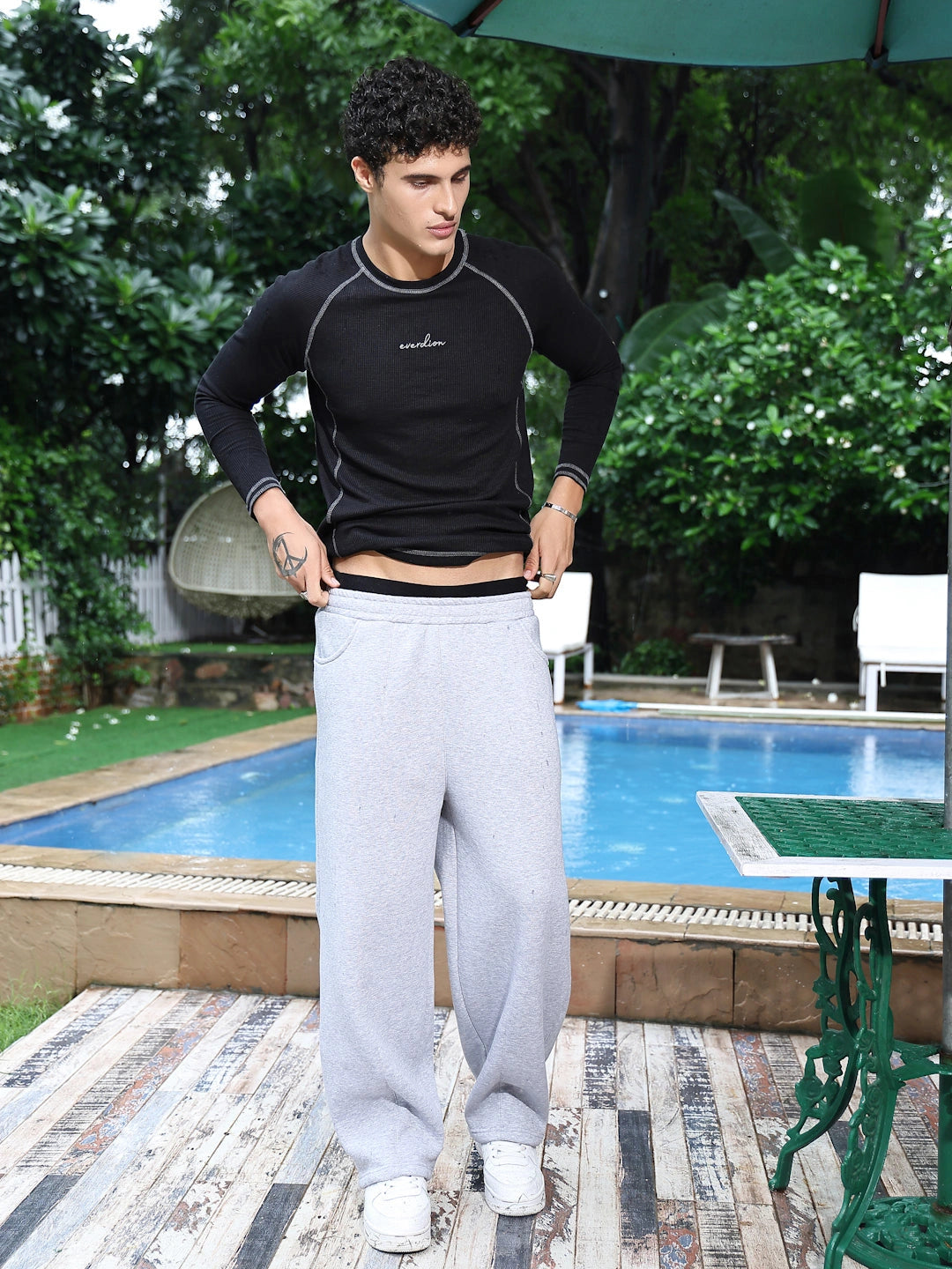 Man in black tshirt and grey sweatpants standing by a poolside.