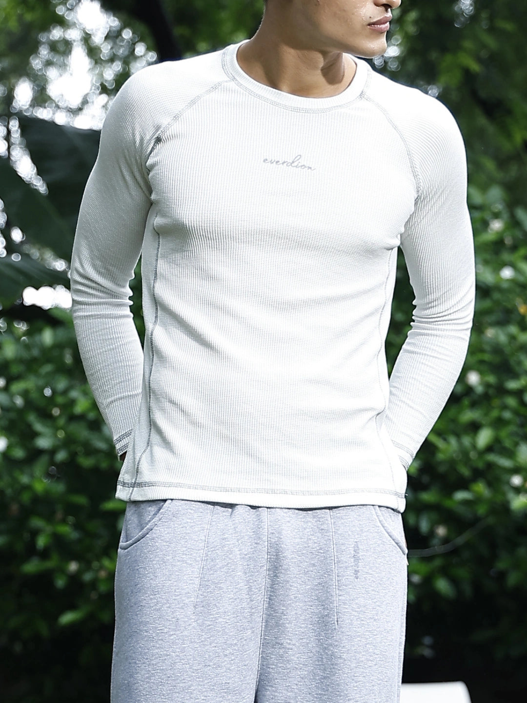 Person wearing a white long-sleeve shirt and grey pants against a blurred green background