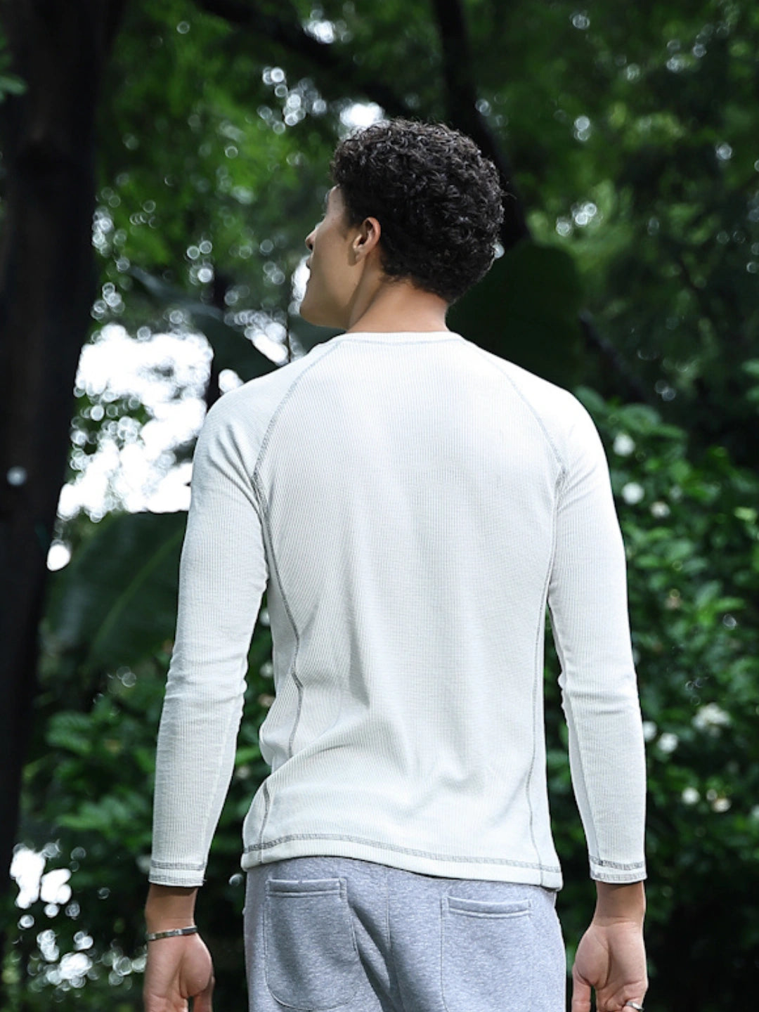 Person wearing a white long-sleeve shirt and grey pants standing in a forested area.