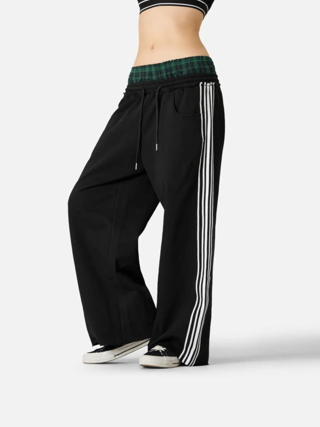 Black track pants with white stripes worn by a person on a white background