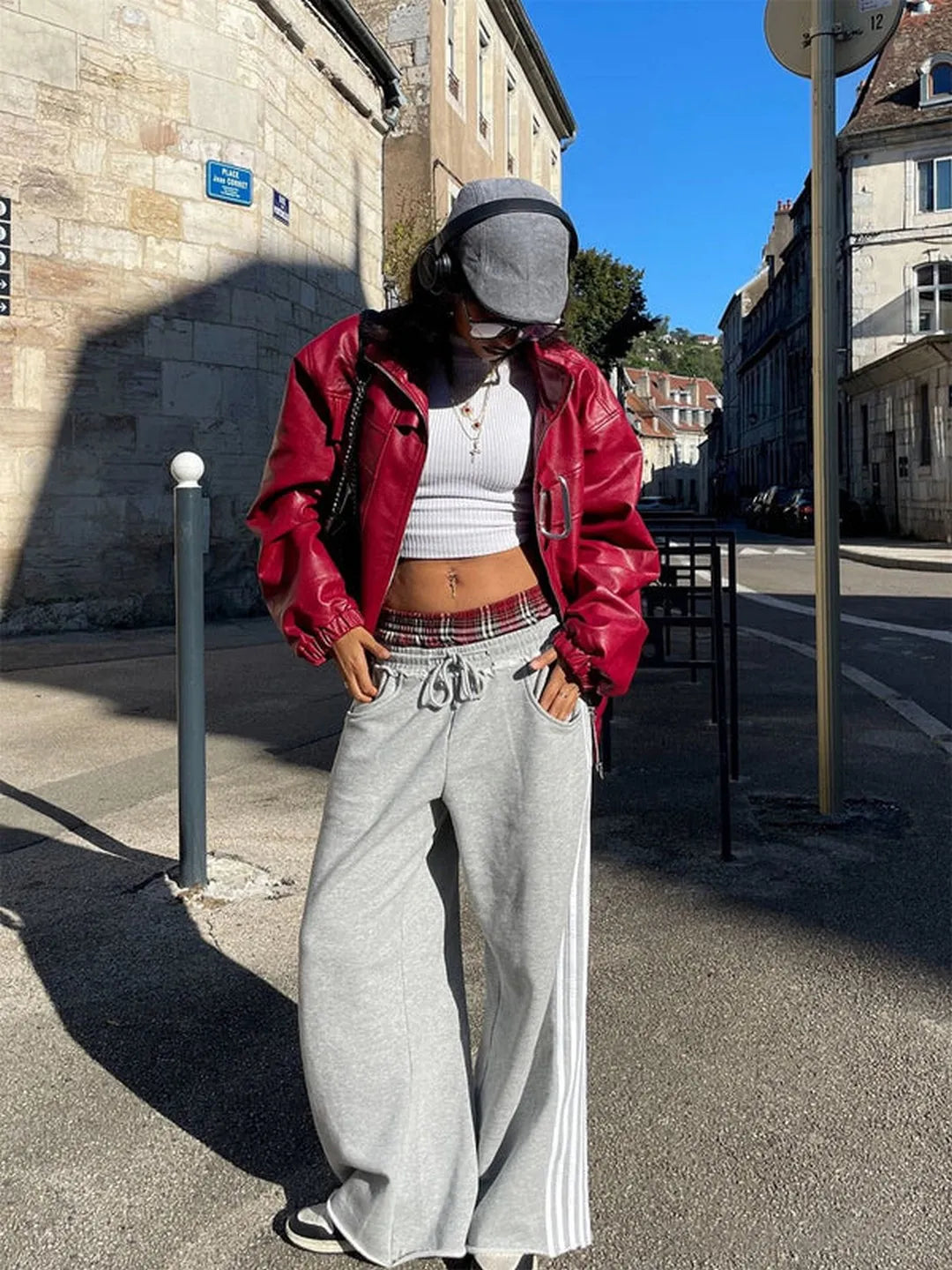 Person wearing a red jacket, white top, and grey pants on a street.