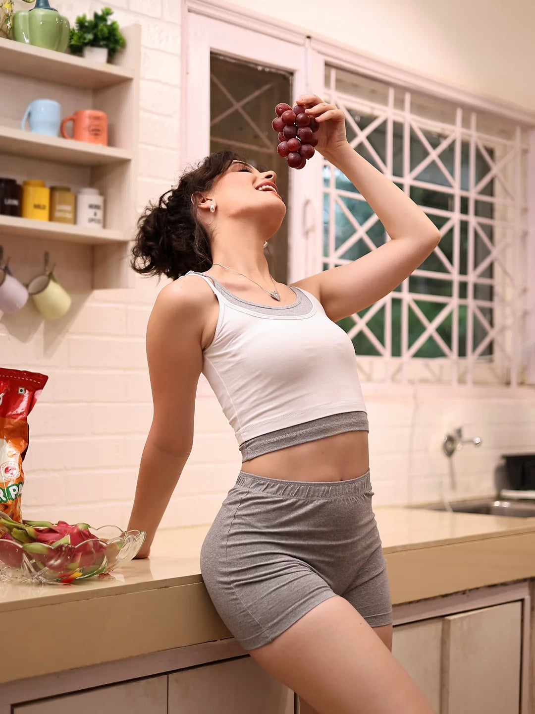 Woman in a kitchen holding grapes above her head
