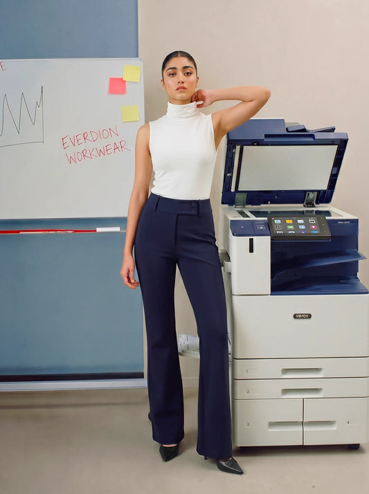 Woman in a white top and navy pants standing next to a printer with a whiteboard in the background.