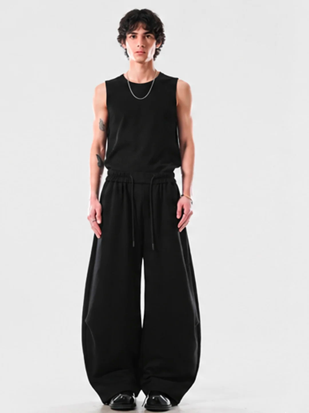 Person wearing a black sleeveless top and wide-leg pants on a white background