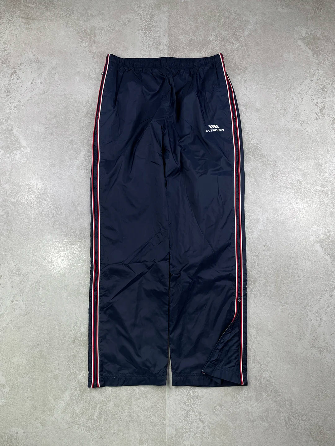 Navy track pants with a red stripe and brand logo on a grey background