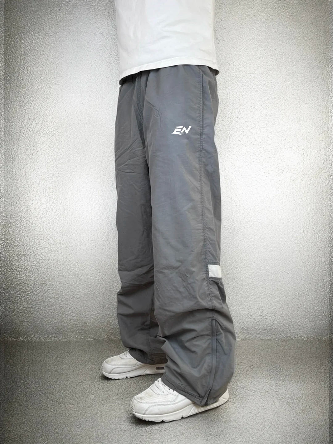 Person wearing grey pants with a logo on a plain background