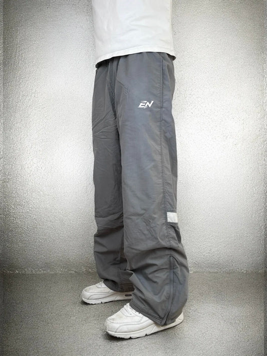 Person wearing grey pants with a logo on a plain background