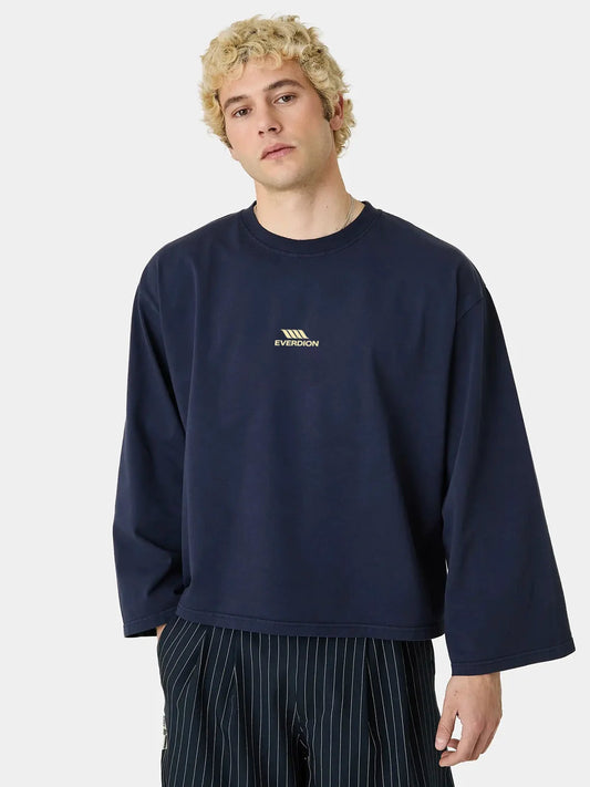 A man wearing a navy blue long-sleeve crewneck t-shirt with a small gold Everdion logo on the left chest, paired with dark pinstriped pants