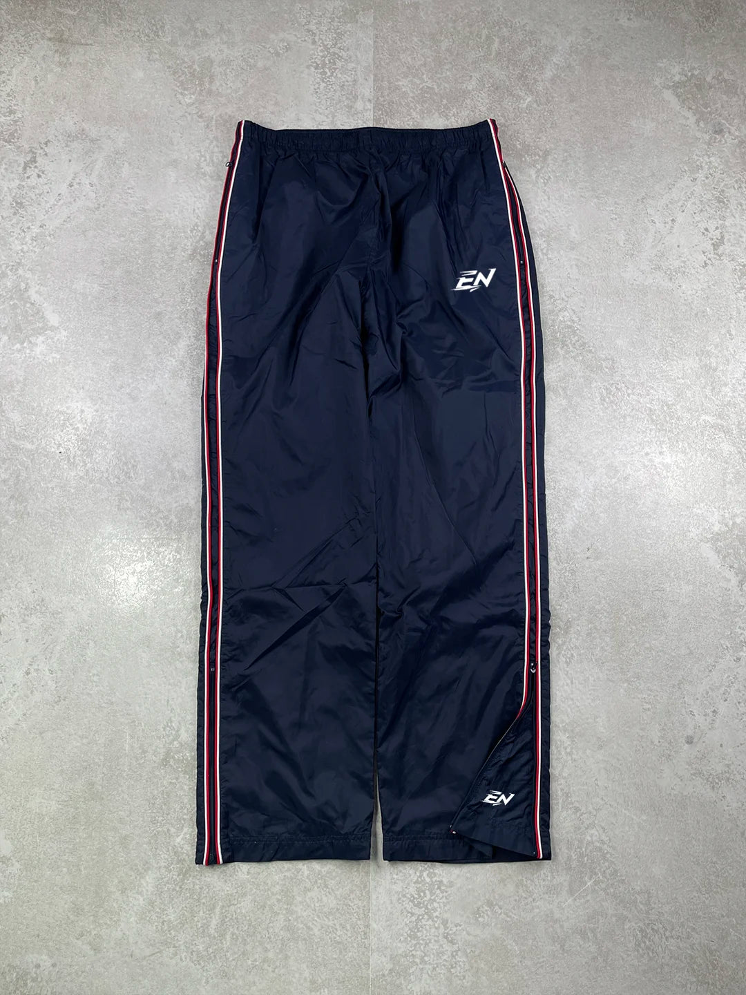 Black track pants with red stripes on a grey concrete surface